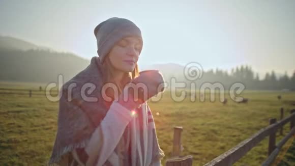 美丽的苗条女士正在秋天的村庄里喝热茶和享受大自然视频的预览图