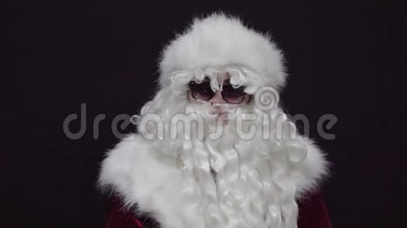 圣诞老人的肖像穿着红色西装戴着太阳镜在黑色背景下以空白的表情看着相机视频的预览图
