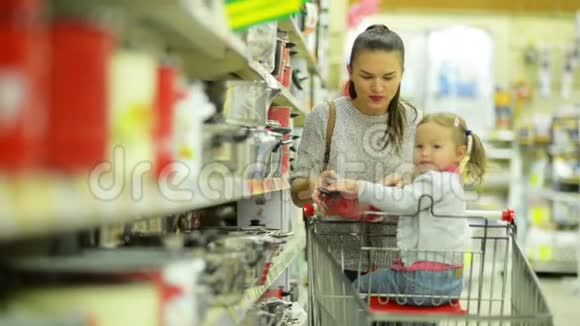 美丽的母亲和女儿在超市里选择一些红盘并把它放在购物车里视频的预览图