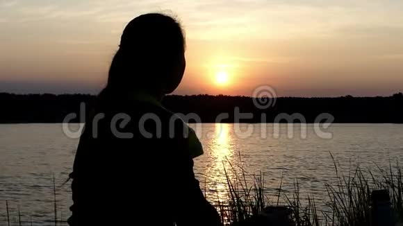 年轻女子坐在湖畔喝热水瓶里的茶视频的预览图