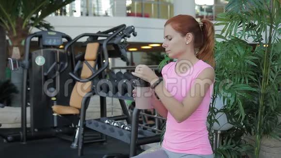年轻女子坐在健身房里喝蛋白鸡尾酒视频的预览图
