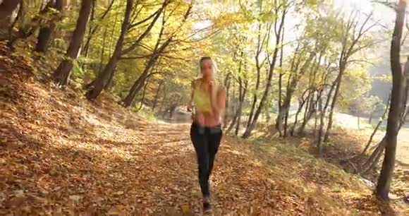 公园里的女跑步者女人在镜头前直勾勾地看着而她却在秋天公园的小径上奔跑视频的预览图