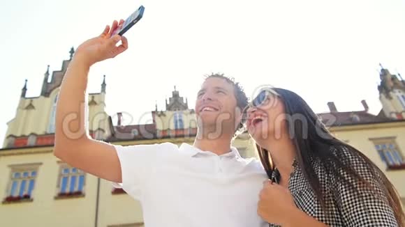 在阳光温暖的背景下快乐的旅行者用智能手机站在旧城广场上视频的预览图