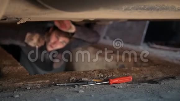 一辆汽车下面的男机修工在车库里用螺丝起子视频的预览图
