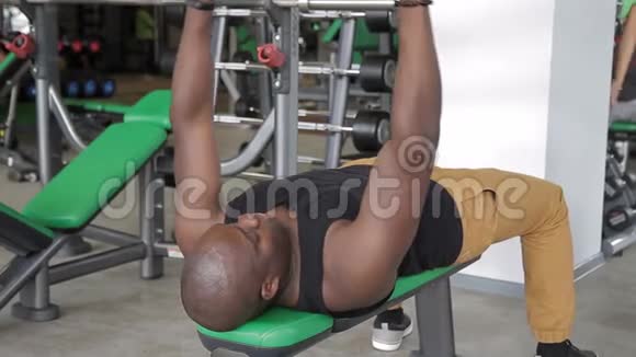 这位美国黑人运动员在训练期间在健身房里做哑铃凳视频的预览图