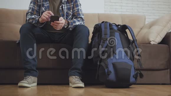 一个坐在沙发上的人在智能手机上使用互联网旁边是一个大型旅游背包视频的预览图