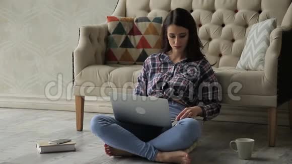 这位年轻女士盘腿坐着在明亮的房间里把她的信用卡号码键入她的笔记本电脑视频的预览图