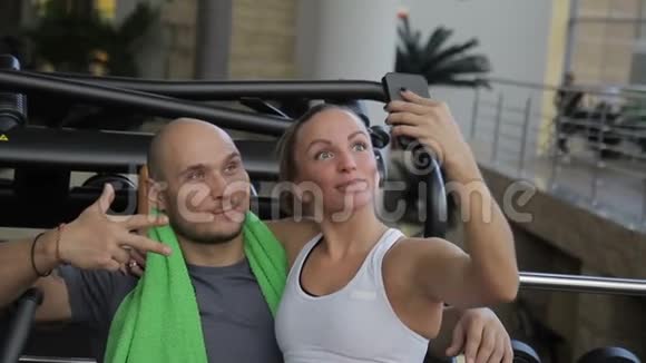 这对幸福的夫妇在健身房休息期间在全新的智能手机上自拍视频的预览图