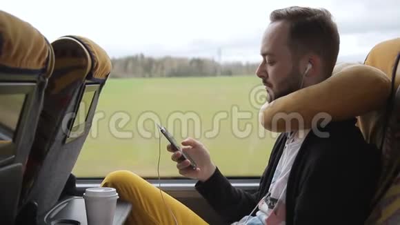 年轻人下午乘公共汽车旅行时拿着智能手机视频的预览图