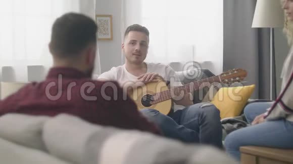 一个男人在他舒适的客厅里和朋友玩吉他视频的预览图