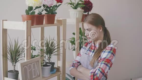 小生意一个穿着条纹围裙和格子衬衫的女孩站在一家花店里架子上有花和一朵视频的预览图