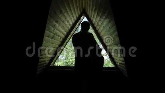 一个男子在一间木阁楼的三角窗前穿上夹克的后景视频的预览图
