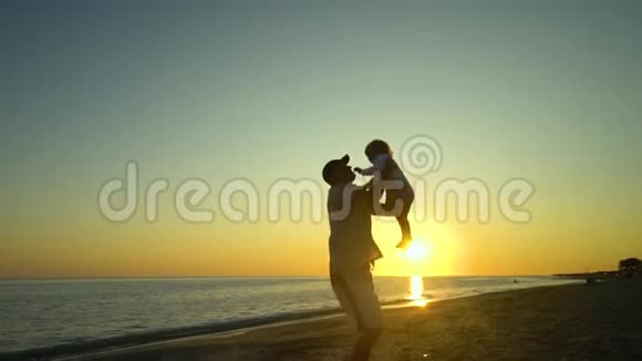 日落时一个年轻英俊的男人和他的小女儿沿着海滨散步爸爸把女儿抱在怀里视频的预览图
