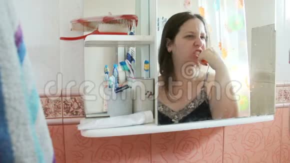 超重长发女人在浴室刷牙穿着蓝色睡衣的女孩倒映在镜子里视频的预览图