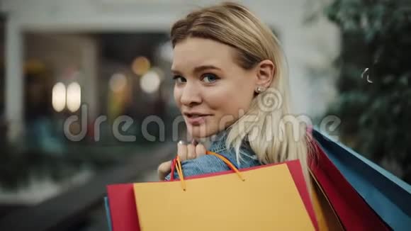 金发女孩看着她的肩膀手里拿着购物袋在商场里散步视频的预览图