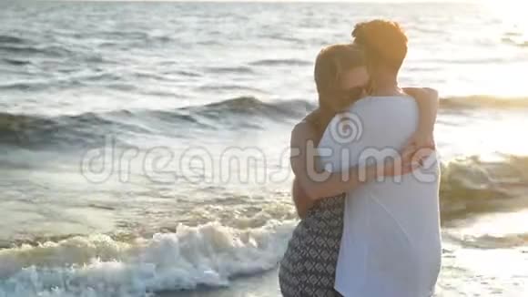 年轻夫妇在波浪背景下的空海滩日落时拥抱视频的预览图