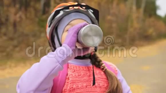 孩子喝铝瓶里的水一个高加索儿童在秋季公园骑自行车小女孩穿黑衣服视频的预览图