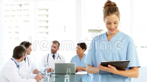 护士在镜头前微笑而工作人员在她身后交谈视频的预览图