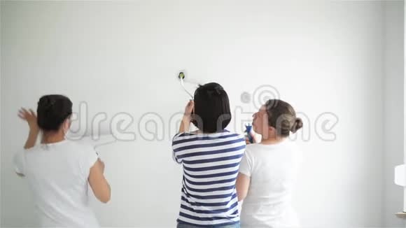 三个快乐的微笑女孩跳舞和画墙在客厅在一起视频的预览图