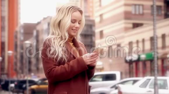 城里的时髦女人微笑和使用智能手机视频的预览图