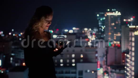 漂亮的女人在窗户附近喝酒和使用智能手机视频的预览图