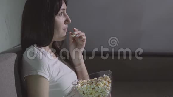 晚上一个年轻的女人独自用爆米花看电影视频的预览图