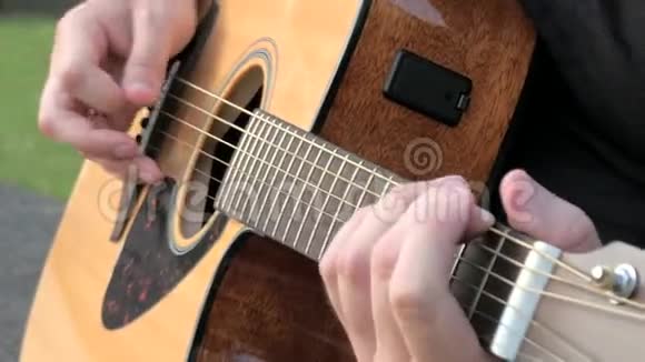 一个在外面弹声吉他的年轻人弹吉他铜弦的人的手音乐家视频的预览图
