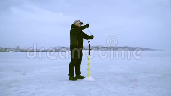 一个渔夫在冬天用冰钻在大自然上钻了一个洞视频的预览图