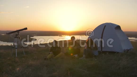 一群朋友坐在帐篷附近的草地上在日落时分畏缩着视频的预览图