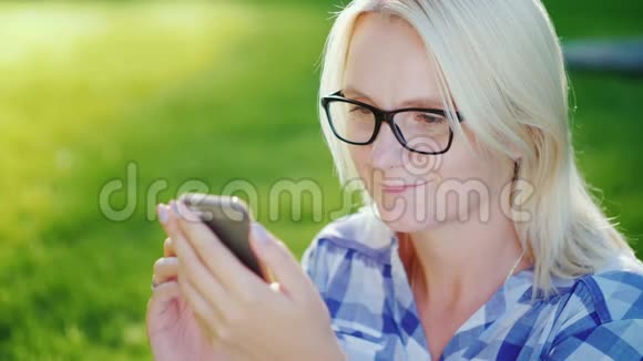 一个女人在晴朗的夏日在公园里休息用智能手机视频的预览图