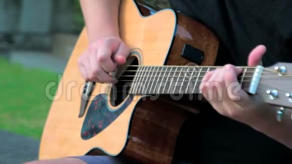 一个在外面弹声吉他的年轻人弹吉他铜弦的人的手音乐家视频的预览图