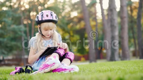 女孩坐在房子附近享受着平板电脑在溜冰鞋上滚动在她的头盔和滚轮上视频的预览图