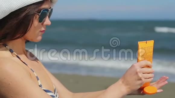 年轻女性在肩膀上涂防晒霜在海边晒太阳视频的预览图