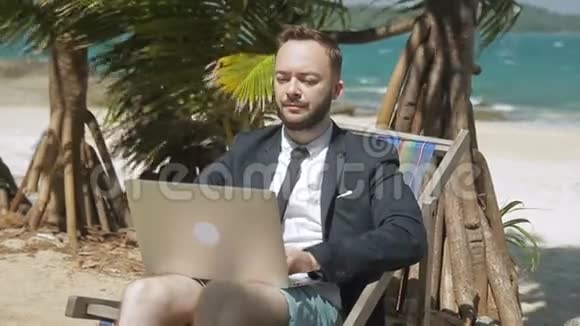 商人正在热带海滩上做他的笔记本电脑视频的预览图