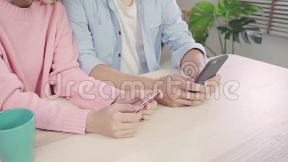 年轻的亚洲家庭夫妇使用智能手机讨论新闻或做网上购物坐在家里的桌子上视频的预览图