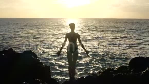 日落时分一个女人在空中观察海浪和举起手臂的剪影电影慢动作视频的预览图