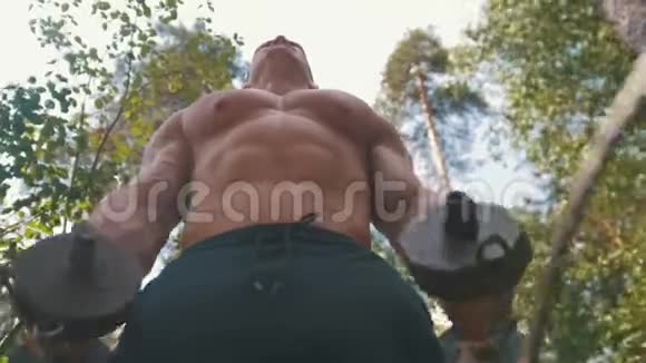 肌肉健美运动员举起一个沉重的铁哑铃在森林中锻炼视频的预览图