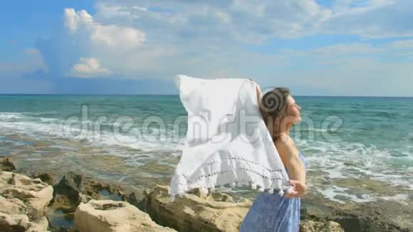 年轻迷人的女人在海边的风中挽着白色的围巾自由视频的预览图