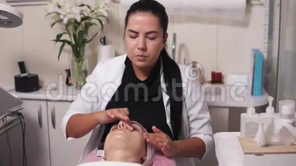 专业美容师正在水疗沙龙做面部按摩年轻女子在撒谎时和她的美容医生交谈视频的预览图