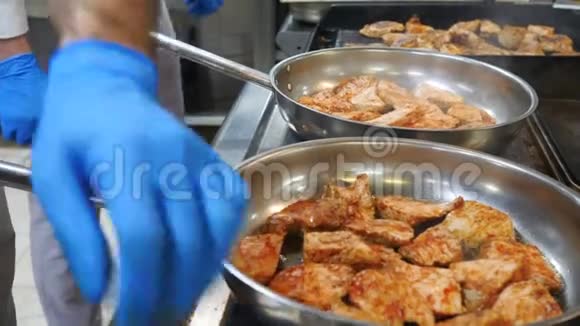 在餐厅的厨房里厨师戴着蓝色手套把肉放在两个煎锅上烤视频的预览图