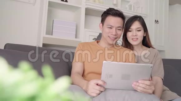 亚洲夫妇使用平板电脑在线购物在家里的客厅甜蜜的夫妇享受爱情的时刻视频的预览图