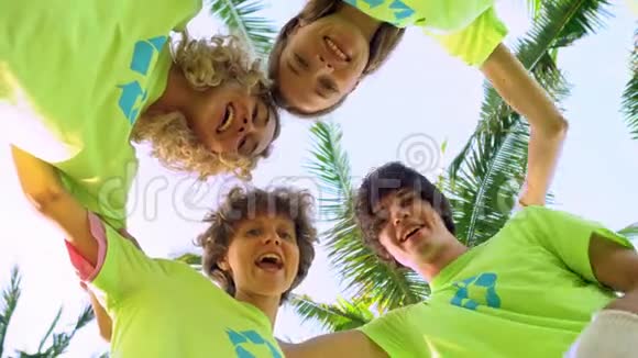 四名年轻志愿者身穿绿色t恤衫照片上的是一个海滩上棕榈树下的一个小丘视频的预览图