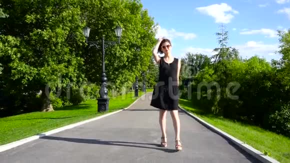 夏天在阳光明媚的公园里穿着黑色连衣裙慢动作快乐微笑年轻女子走来走去视频的预览图