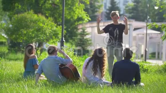 夏天公园里年轻人坐在草地上在朋友面前表演哑剧视频的预览图