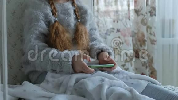 快乐的小女孩戴着耳机的辫子用电话玩微笑坐在房间的窗台上视频的预览图
