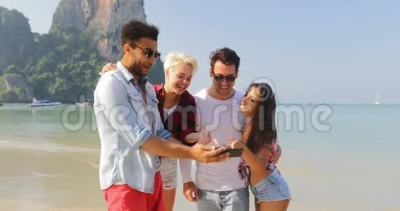 人们在海滩上使用手机观看照片两对情侣在度假时拥抱快乐的男女游客视频的预览图