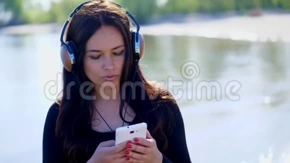 夏天河边海滩上日出时美丽的女人留着长长的黑发听着耳机里的音乐视频的预览图