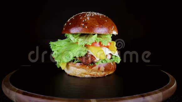 汉堡里有一大块肉青菜和奶酪正在黑色背景的木板上旋转视频的预览图
