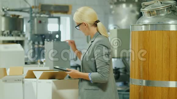 一个带着平板电脑的女人在成品仓库里做存货附近有几箱酒和一大箱酒视频的预览图