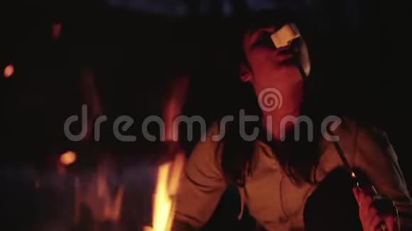 布鲁内特女孩在篝火旁煎棉花糖微笑着晚上休息视频的预览图